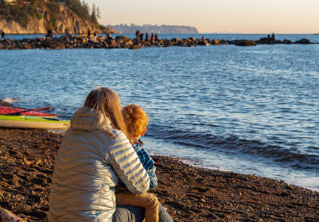 A woman and a child at the seashore on a autumn day. Small boy and his mother are embracing at the seashore watching sunset. Selective focus, blurred background, copyspace for text.の写真素材