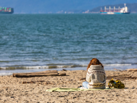 Woman sitting alone on the sand and enjoying the sunshine. Back view, copy space for text, travel photoの写真素材