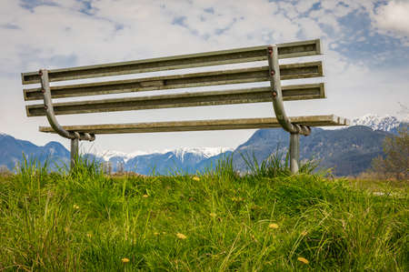Empty bench in the park with green fresh grass. Park bench at the blue sky and clouds in the background, concept for a bench in heaven, a place to relax. Nobody, travel photo, copy space for textの写真素材