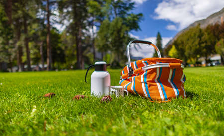 Summer picnic on the green grass. Tea pot flask  and baskets of food for the outdoor picnic in a park on the blue sky and clouds in the background. Street view, travel photo, nobody.の写真素材