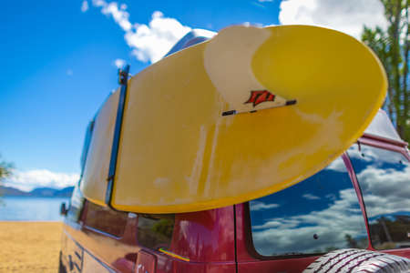 Camper van with colorful surf board on a sunny summer day at the beach. Vintage car parked on the beach or seaside with a surfboard on the side. Leisure trip in the summer. Travel photo, nobodyの写真素材