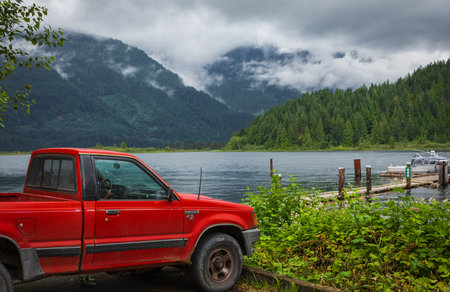 Red pickup truck parked on a lakeside with mountains in the background on early moody morning. Beautiful natural landscape Pitt Lake BC Canada. Travel photo, nobody, selective focusのeditorial素材