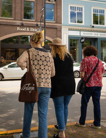 Rear view shot of three women walking together on city street. Female friends out on the street on a...