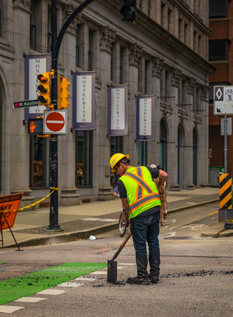 Team of workers put the hot asphalt on a road. Road construction workers with shovels in protective uniforms. Road Construction Works in a city-July 10,2022-Vancouver Canada. street photoのeditorial素材
