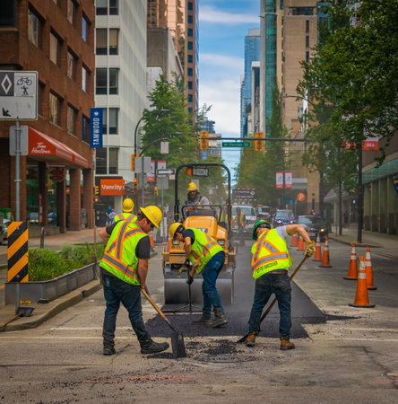 Team of workers put the hot asphalt on a road. Road construction workers with shovels in protective uniforms. Road Construction Works in a city-July 10,2022-Vancouver Canada. street photoのeditorial素材