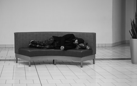 Homeless man is sleeping on a bench in the mall. Homeless beggar man lying on bench indoors, sleeping-december 8,2022-Surrey BC Canadaのeditorial素材