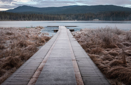 Wooden pier on lake site facing a beautiful mountain on a misty winter morning. Cold winter morning on a forest lake. Frosty calm landscape. Natural tranquil atmosphere for relaxationの写真素材