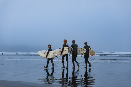 Surfers carrying surfboards running on the beach early morning for a surf. A surfers with their...
