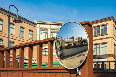 Outdoor convex safety mirror hanging on wall with reflection of an urban roadside view by residential apartment buildings. Round mirror on a post to help cornering transport. Nobody, street photoの写真素材