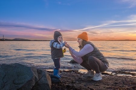 A woman with her child at a beach on a cold day. Mother with her child on the beach during sunset. Little boy and his mother playing on the beach-Vancouver Canada-January 10,2023-copy space for textのeditorial素材