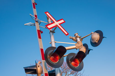 Railroad crossing traffic sign with red lights and barrier lowering indicating that a train is...
