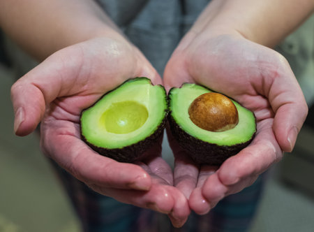Avocado in heart shape in hands of a woman. Top view of fresh sliced avocado. Vegetarian food...