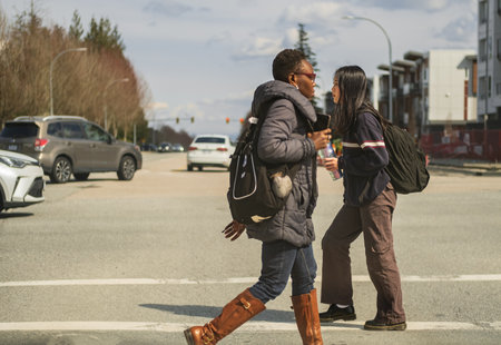 People walking at the traffic lights to cross busy road. Asian young woman and stylish african...