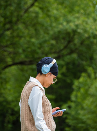 Young girl using phone to listen music on her headphones in the park. Technology wireless headphones...