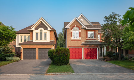 Real Estate Exterior Front House on a sunny day. Big custom made luxury houses with nicely landscaped front yard and driveway to garage in summer in the suburbs. Beautiful house entrance with a gardenの写真素材