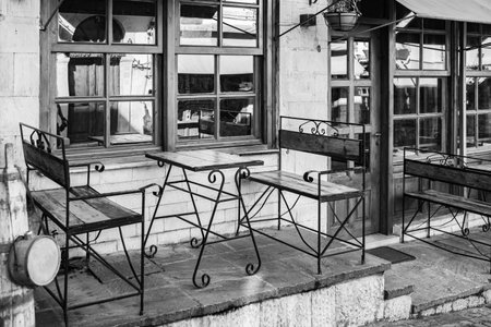 Old fashioned cafe terrace in black and white. Cozy old street in Gjirokaster Albania. Outdoor cafe with wooden tables and chairs. Nobody, street photo, selective focusの写真素材