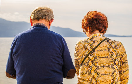 Rear view of a senior couple sitting on a wooden bench in the park. Elderly couple in the park on sunny day. Senior Retired couple sitting on the bench. Close up view.の写真素材