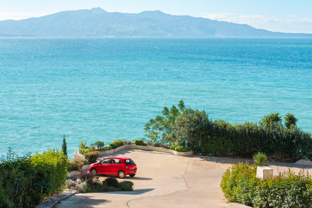 Car on a sea coast. Red car on the road near the ocean on sunny summer day. Red car parked at the beach. Summer vacation at the beach. Summer travel by car. Road trip. Automotive industry.の写真素材