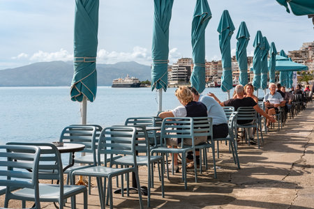 Sea view with eating people in a restaurant with terrace along the coast in Saranda Albania. Street view of a outdoor waterfront terrace with tables and chairs in restaurant-November 1,2023のeditorial素材