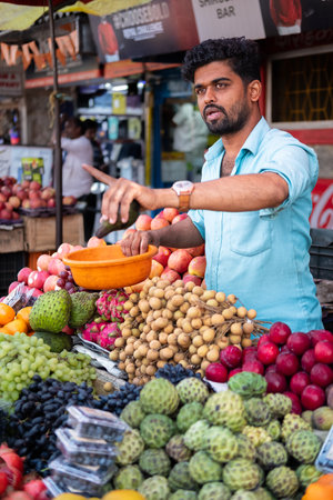A young Indian man sells fruits at his shop in a local market Goa India. Man selling vegetables and fruits to customers in a market in Goa Bazar. Street view, travel photo-Jan 30,2024のeditorial素材