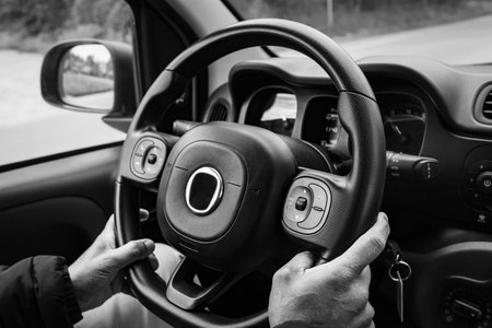 Hands on steering wheel of car driving on highway. Man holds the steering wheel firmly with both...