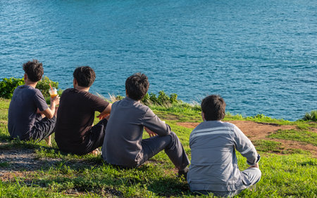 Back view Group of young Asian men friends sitting together on summer holiday vacation in green...