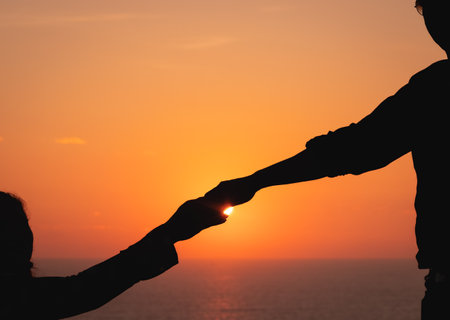Hands of the young couple in love during sunset. Close up of diverse couple holding hands at beach...