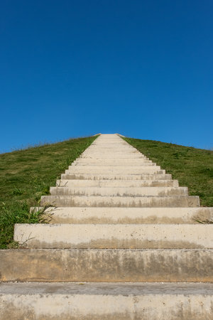 Long Staircase Leading Up a Green Hill Under Blue Sky. Concrete steps leading up a grassy hill on a sunny day. Vertical photo. Nobody, copy space for textの写真素材