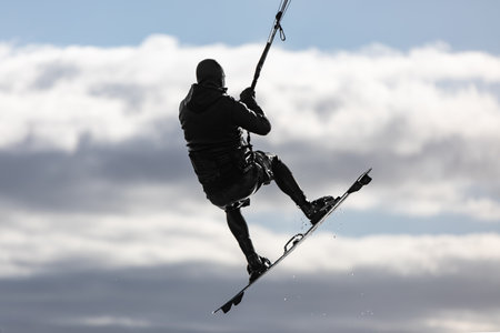 Kite surfer flies over the sky. Kite boarder is gliding on high speed jumps over water. Men in black wet suits go kitesurfing. Extreme sports, kiteboarding. Editorial-Oct 30,2020の写真素材