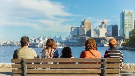 Family sitting on a bench at Stanley park watching the Vancouver Skyline. Beautiful sunny day in Vancouver British Columbia Canada. Travel concept, copy space.の写真素材