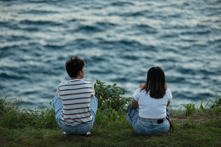 Young couple watching sunset by the sea enjoying seascape Phuket Thailand. Rear view of Asian couple sitting in a park at summer day. Active adventure, travel, tourism, lifestyle concept-July 8,2024の写真素材