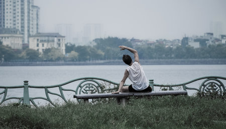 Man stretching in the park on the bench in front of a lake. Young man workout before fitness training at the park. Healthy and exerciseの写真素材
