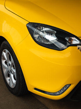 Close-up of the front headlight and wheel of a yellow modern car. Headlight on yellow car, front view, close up. Headlamps of a vehicle. Nobody, street photoの写真素材
