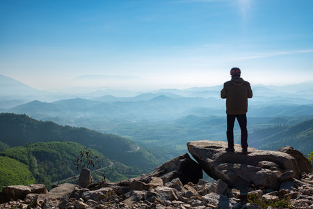 Man on stone on the hill and beautiful mountain valley in Vietnam. Traveler stands and enjoys valley view from hilly viewpoint. Traveling on hill peaks landscape. Sport, tourism and hiking concept.の写真素材