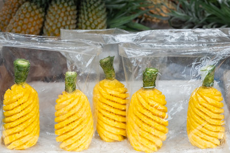 Ripe pineapple peeled in plastic bag selling in local market. Whole ripe pineapple peeled. Nobody, street photo. Delicious peeled pineapples in plastic bags with wooden stick for sale.の写真素材