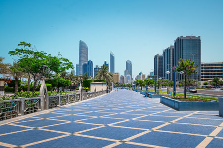 Beautiful walkway in urban city park with green trees. View of the Corniche promenade in Abu Dhabi, UAE. Corniche boulevard beach park along the coastline. Travel photo, Summer vacation conceptの写真素材