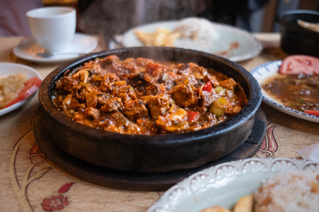 Traditional delicious Turkish food with meat and vegetables roasted in cast iron pan. Lamb stew served in a rustic style on a table in restaurant. Soft focus, nobodyの写真素材