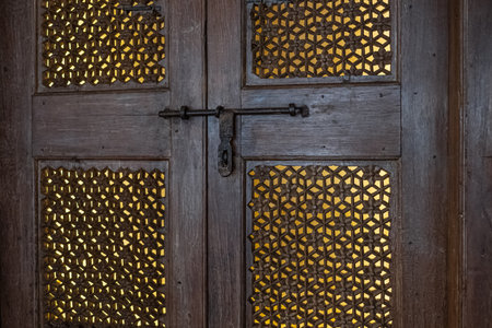 Close-up double wooden door with a black metal latch. Traditional double wooden door with iron latch and unique carved ornaments in old homes in India. Rustic, vintage wooden door with decorated frameの写真素材