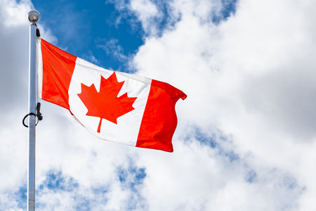 Canadian Flag blowing on a blue sky windy day. The Canadian flag flying against the blue sky on a metal flagpole. Flag of Canada in red and white with red maple leaf in the center.の写真素材