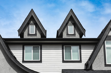 Facade of the house with nice window. Top of the wooden home. The roof of the house with nice window. Home exterior with blue sky on the background. Attic apartments background. House garret closeupの写真素材