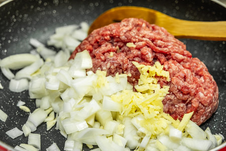 Close up raw ground beef with chopped onion in a pan and wooden spatulate. Minced meat with fresh onion on frying pan, top view. Homemade cooking process and fresh ingredients concept.の写真素材