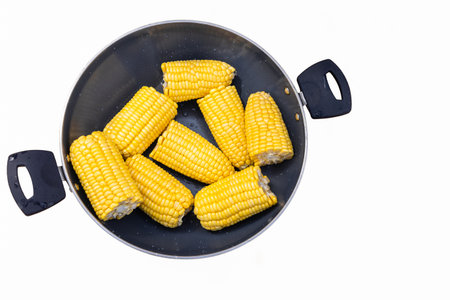Boiled corn cobs. Fresh yellow boiled corn cobs halves in a pot, viewed from directly above on white...