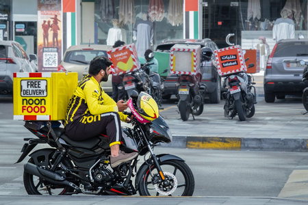 Motorcycle driver delivers food delivery. Delivery man Noon Food. Delivery rider on the street Abu Dhabi UAE. Express food delivery service-Apr 19,2025のeditorial素材
