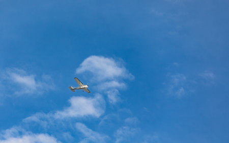 Small Plane flies in blue sky. Private jet plane flying at high altitude among white clouds in the...