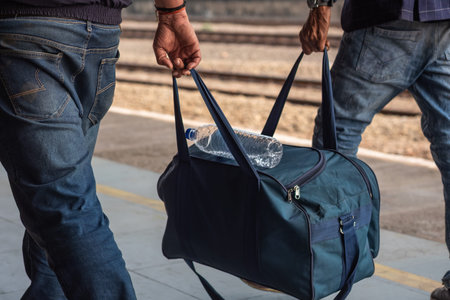 People with travel bags walking on the station. Rear view of two unrecognizable men carrying a heavy...