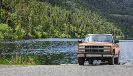 Orange color 4x4 Offroad Pickup truck on the road along the mountain river and forest. Front view of...