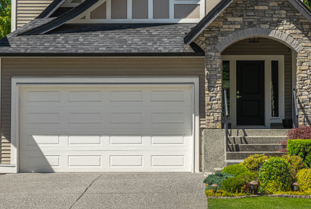 New wide roll up garage door and concrete driveway of a residential house. Real Estate Exterior Front House with nicely landscaped front yard and driveway to garage in the suburbs of Vancouver Canada