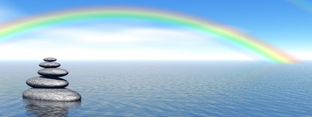 Balanced grey stones in the deep blue ocean with a beautiful rainbowの写真素材