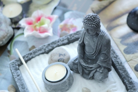 Grey stone buddha in front of a small yellow candle on a zen tableの写真素材
