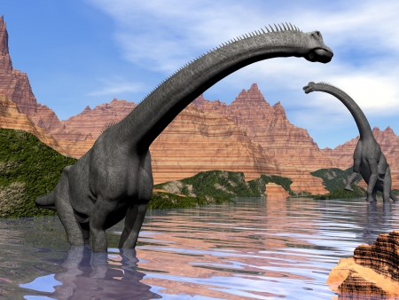 Two brachiosaurus dinosaurs in water next to red rock mountains by beautiful dayの写真素材